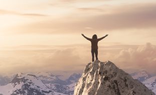 Adult,Adventurous,Woman,Standing,On,Top,Of,A,Snow,Peak.